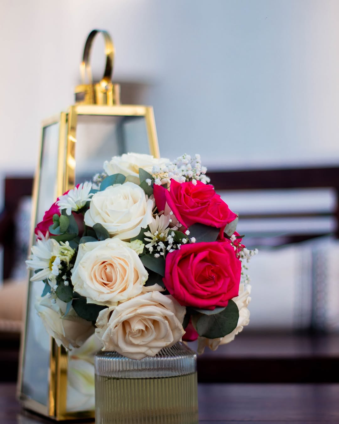 Detalle floral con rosas en tonos crema y fucsia junto a farol dorado