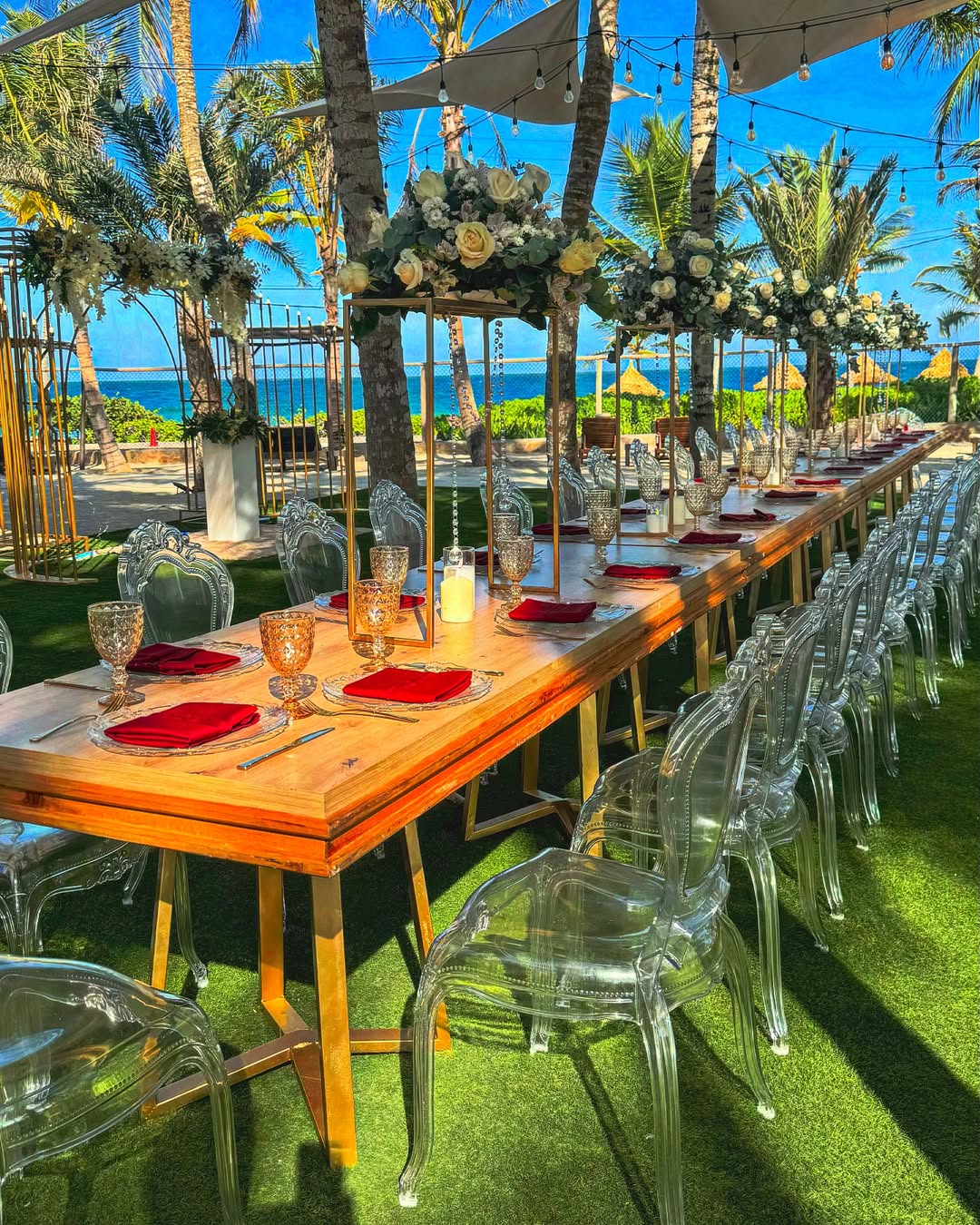 Banquete frente al mar con mesas de madera, sillas transparentes y florales elevados