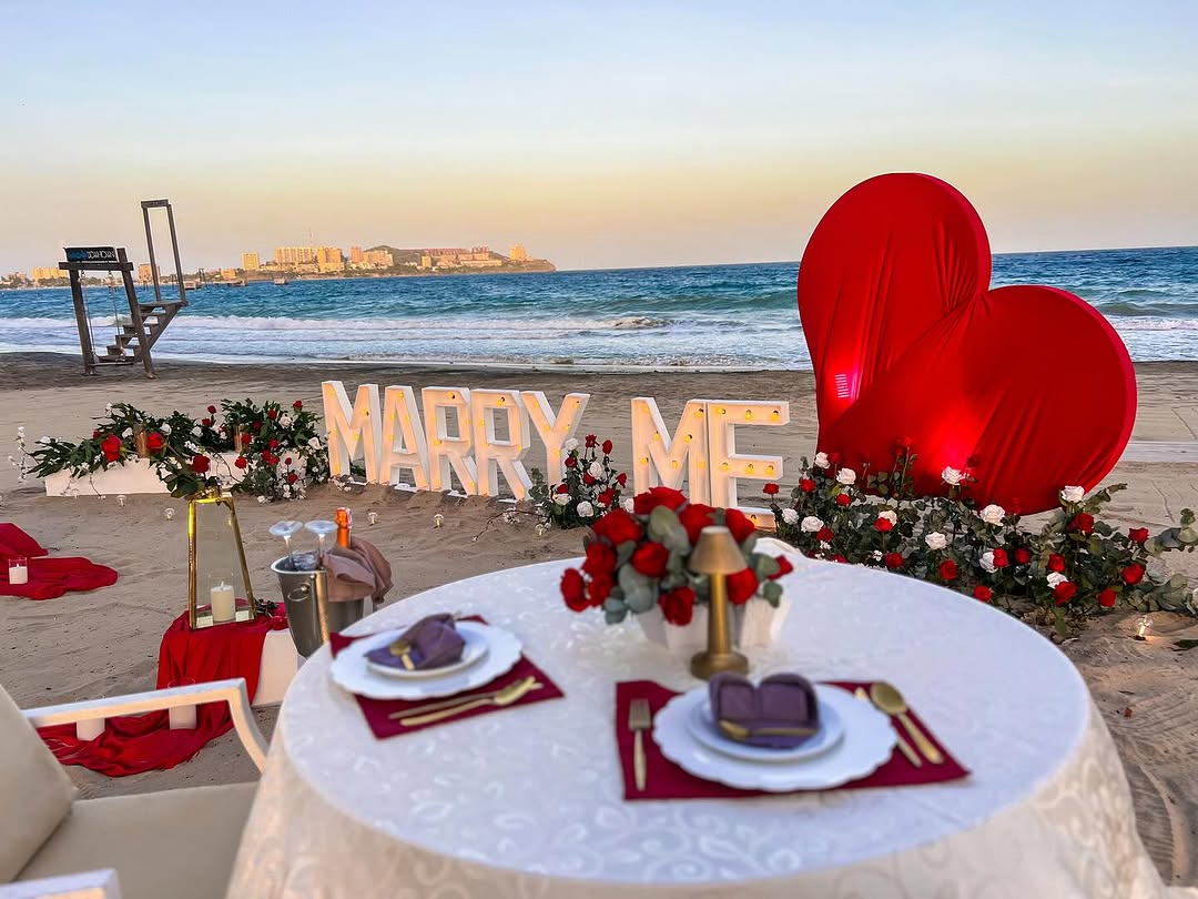 Pedida de mano romántica con velas y flores rojas frente al mar